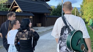 Vier Menschen laufen über eine Dorfstraße in der Slowakei und sprechen miteinander. Einer von ihnen trägt eine grüne Gitarre auf dem Rücken.