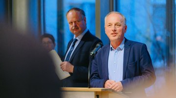 Der Landesvorsitzende steht in Jackett und Hemd gekleidet im Innenraum des Landtages vor einer Fensterfront an einem Pult und spricht zum Publikum.